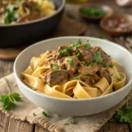 Vegan beef stroganoff with creamy sauce over wide pasta noodles, garnished with fresh parsley.