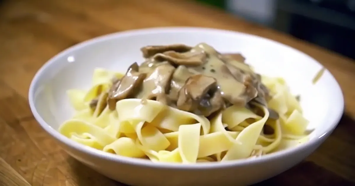 Vegetarian Beef Stroganoff served over fettuccine with mushrooms and vegan beef strips, garnished with fresh parsley in a ceramic bowl.