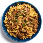 Vegetarian Beef Stroganoff served over fettuccine with mushrooms and vegan beef strips, garnished with fresh parsley in a ceramic bowl.